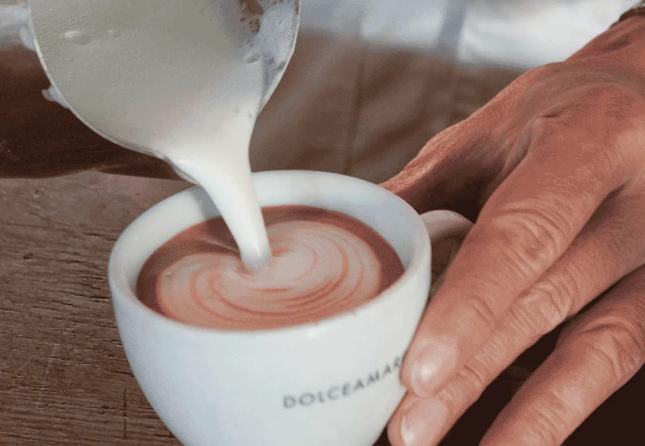Milch wird in eine Tasse mit dem Schriftzug Dolce Amaro gegossen