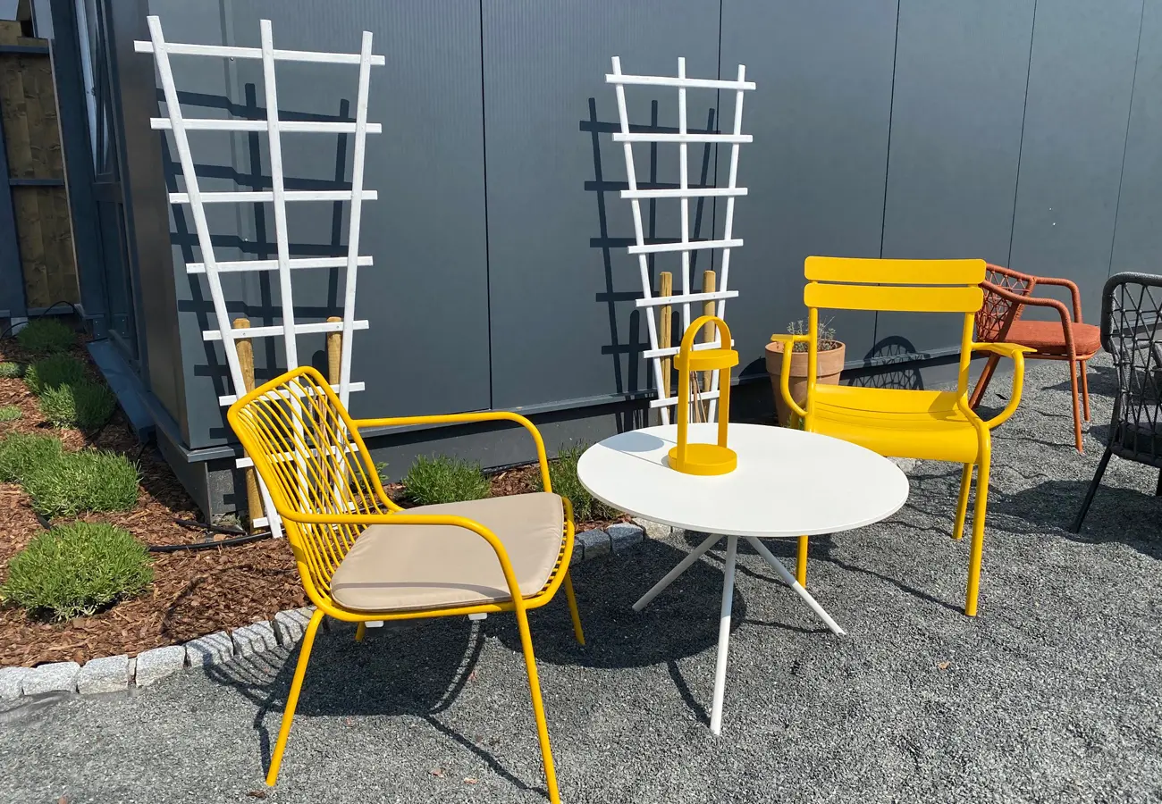 Gelbe Gartenstühle um einen weißen Tisch vor Rankgittern