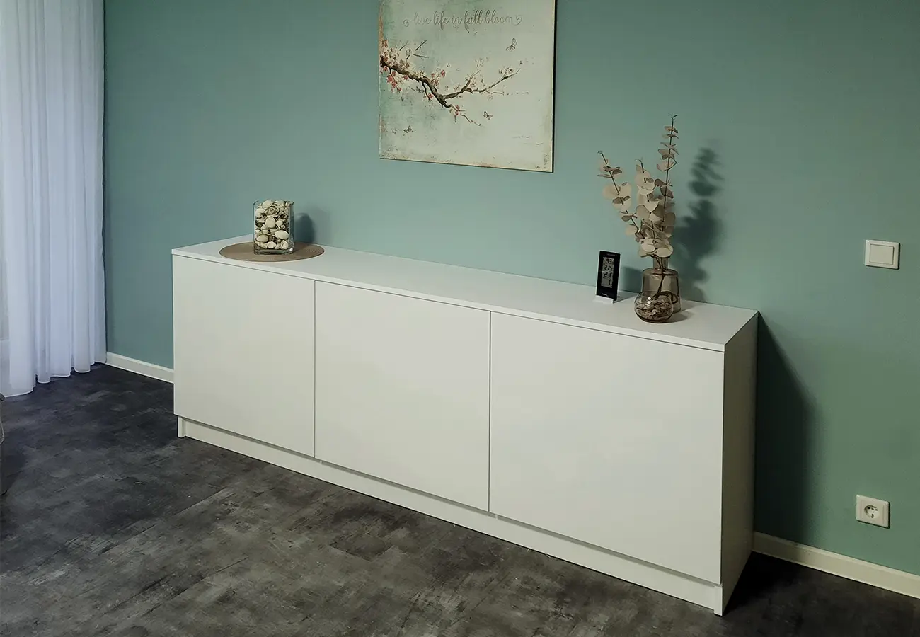 Weißes Sideboard vor grüner Wand im Wohnzimmer