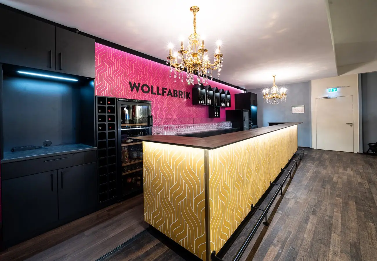 Bartheke mit goldener Musterfront vor pinkfarbener Wand mit dem Schriftzug Wollfabrik